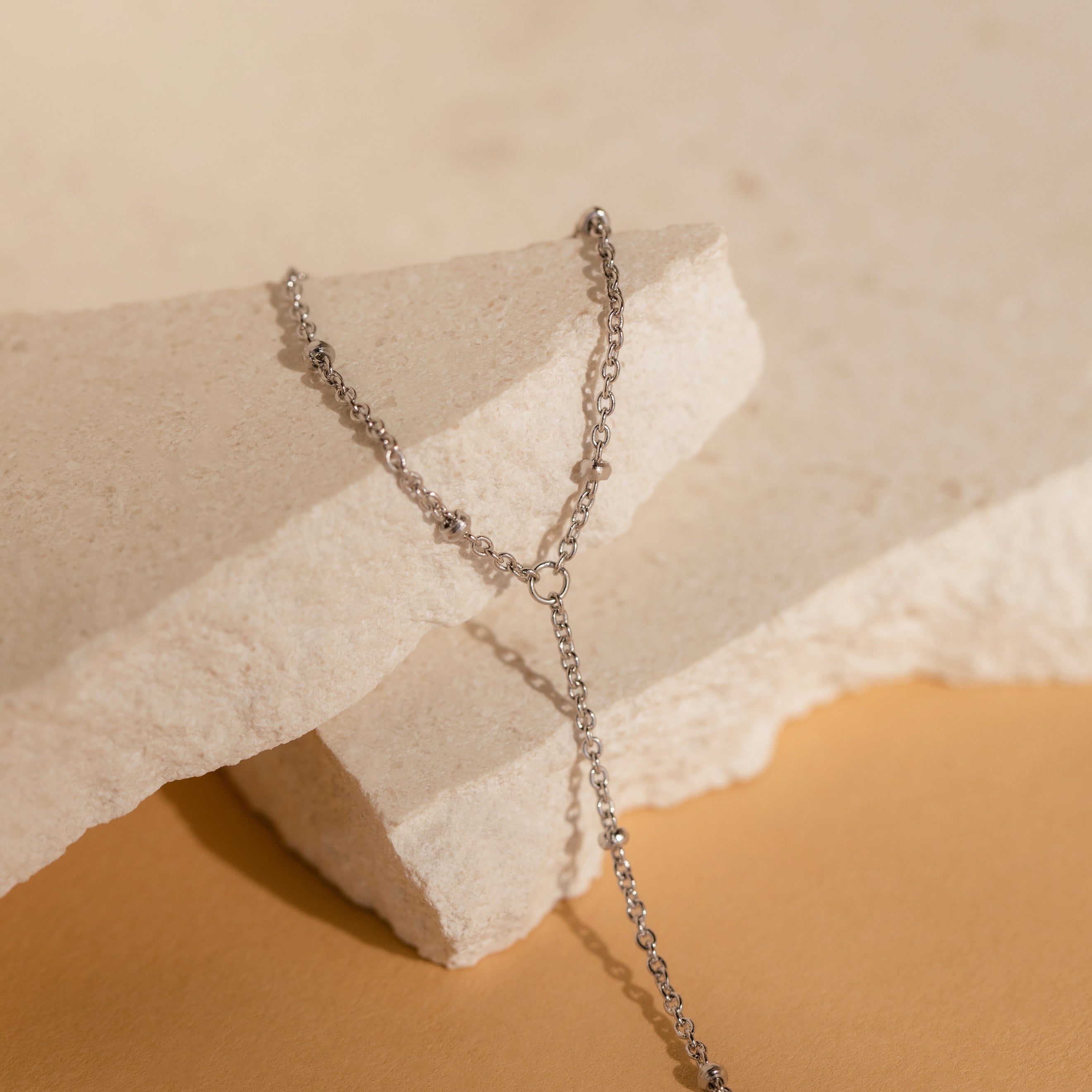 The Beaded Hand Chain Bracelet in Sterling Silver, a stunning statement piece, is elegantly showcased on textured, light-hued stone.