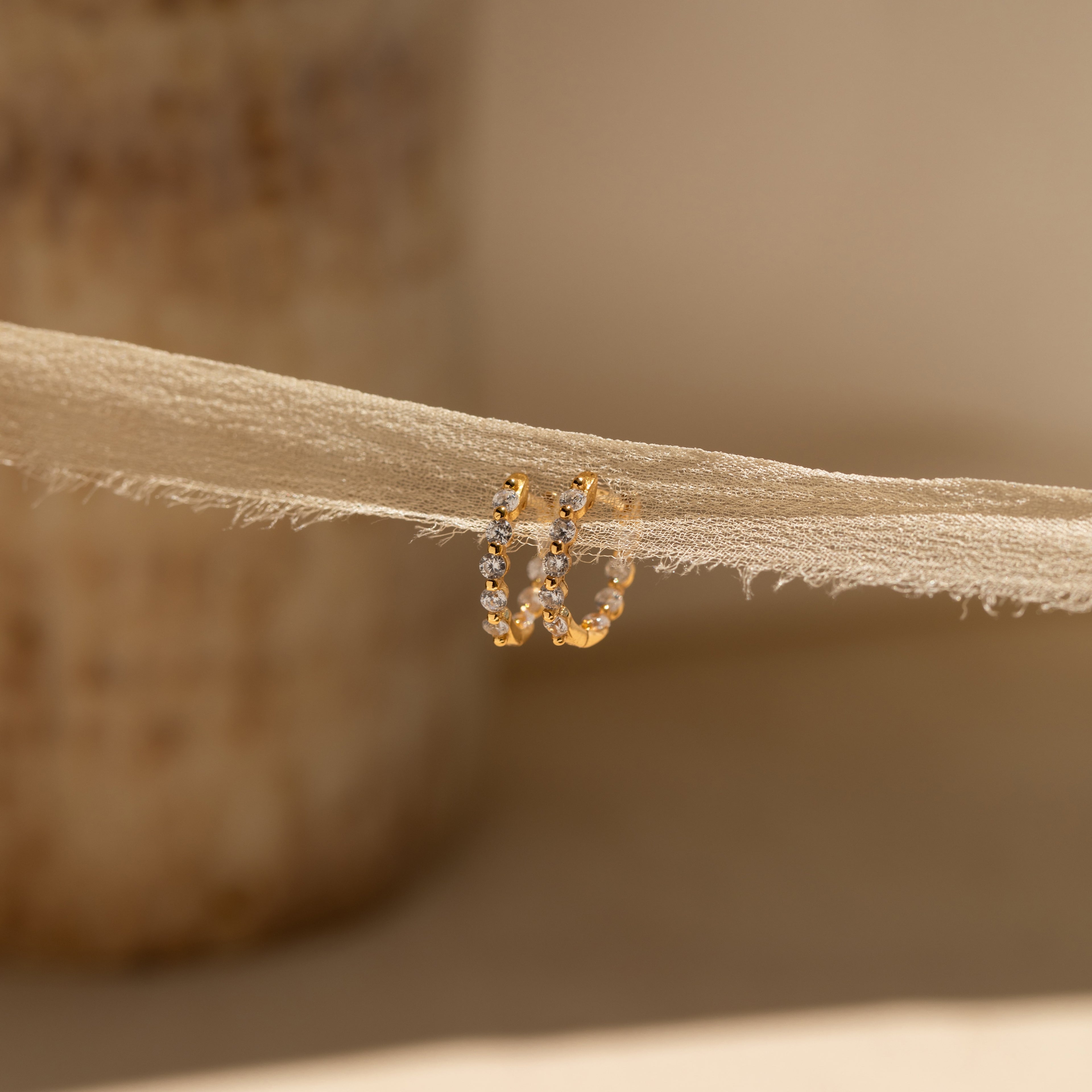 Inside Out Diamond Huggies featuring sparkling diamonds, shown on beige fabric and softly illuminated by natural light.