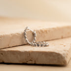 The Inside Out Diamond Huggies in Sterling Silver sparkle with diamonds as they rest atop stacked beige stone slabs, reflecting light from every angle.