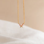 Pink Opal Butterfly Necklace in 18K Gold, featuring a delicate butterfly charm, photographed on a soft beige and white background.