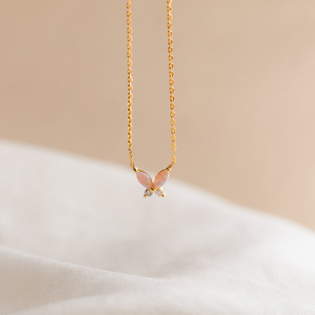 The Pink Opal Butterfly Necklace showcases a delicate butterfly pendant on gold, photographed against a soft beige background—a charming gemstone necklace for any occasion.