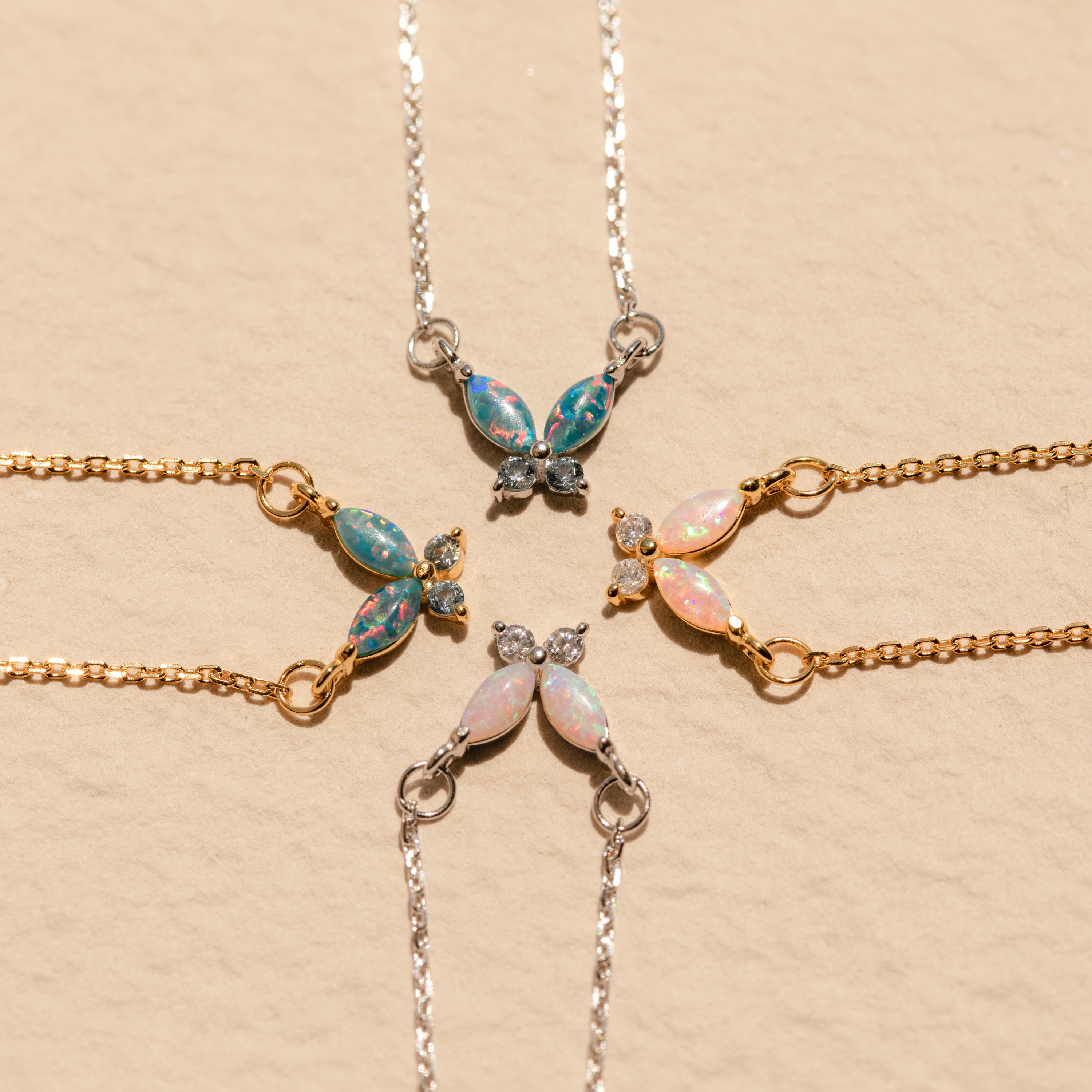 Four butterfly-shaped gemstone bracelets in gold and silver are arranged in a circle on beige, perfectly complementing the Pink Opal Butterfly Necklace.