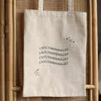 The CM Tote Bag is a chic, beige minimalist tote featuring "CAITLYNMINIMALIST" text repeated three times with heart and star illustrations—perfect for versatile, everyday style.