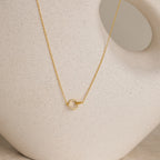 The Pave Interlocking Necklace in 18K Gold features a small circle pendant, elegantly displayed against a cream ceramic vase—ideal as bridal jewelry or a meaningful unity necklace.