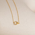 The Pave Interlocking Necklace in 18K Gold features a delicate chain with a small, circular gemstone pendant—perfect as elegant bridal jewelry on a light surface.