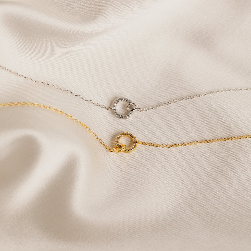 The Pave Interlocking Necklace, perfect unity or bridal jewelry, is elegantly displayed on smooth cream satin fabric.