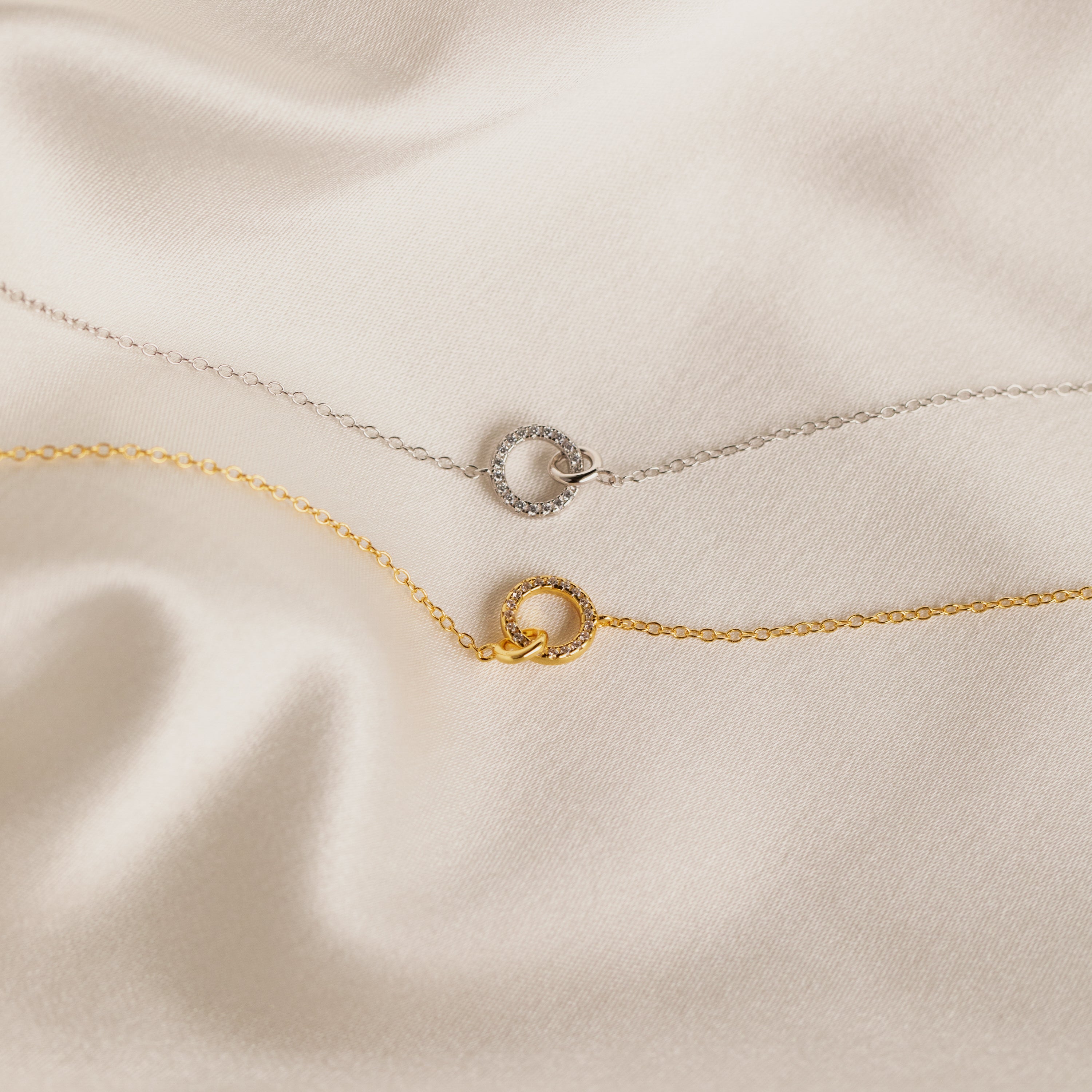 The Pave Interlocking Necklace, perfect unity or bridal jewelry, is elegantly displayed on smooth cream satin fabric.