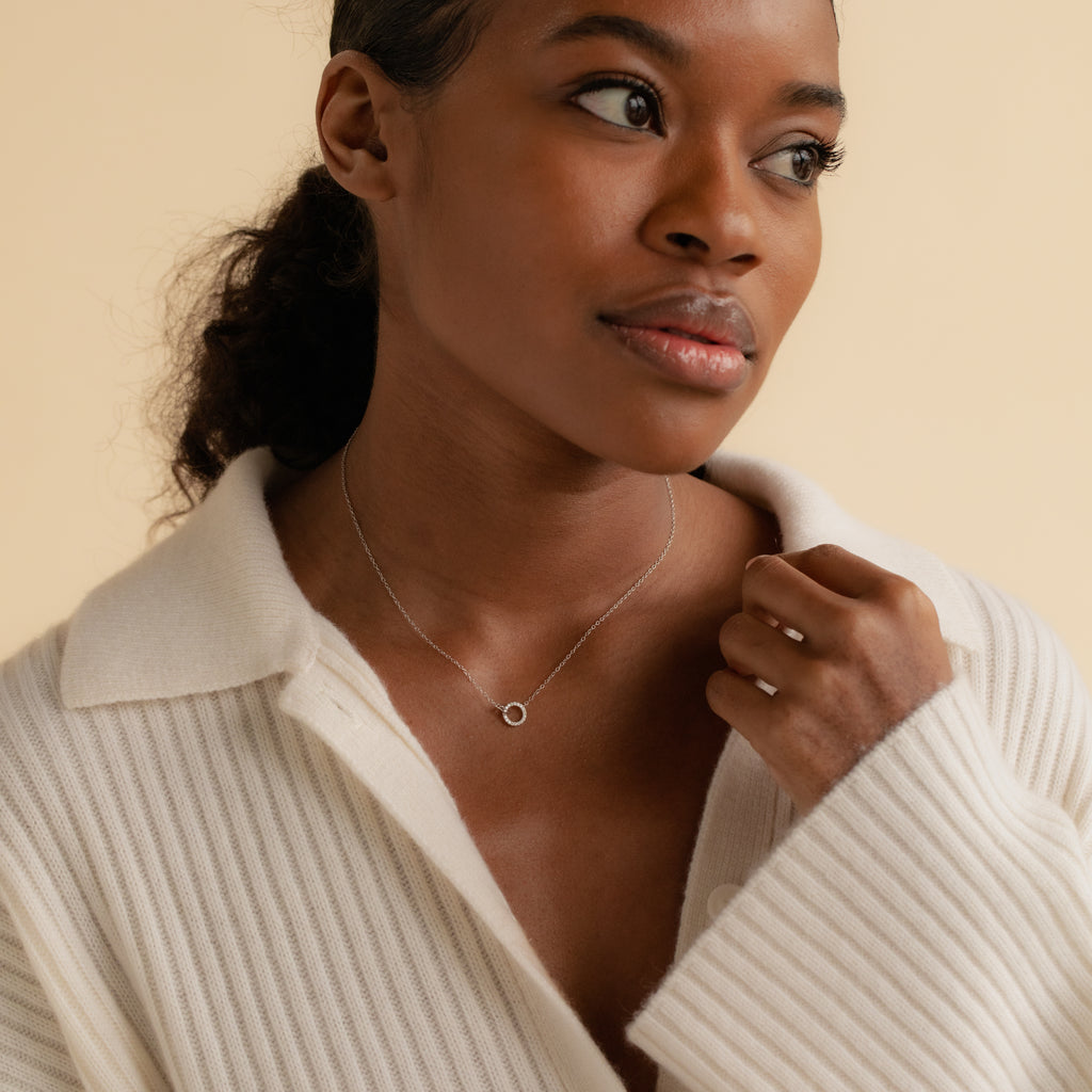 Woman wearing a cream ribbed sweater and the Pave Interlocking Necklace in Silver, looking thoughtfully to the side—an elegant keepsake perfect for bridal jewelry moments.