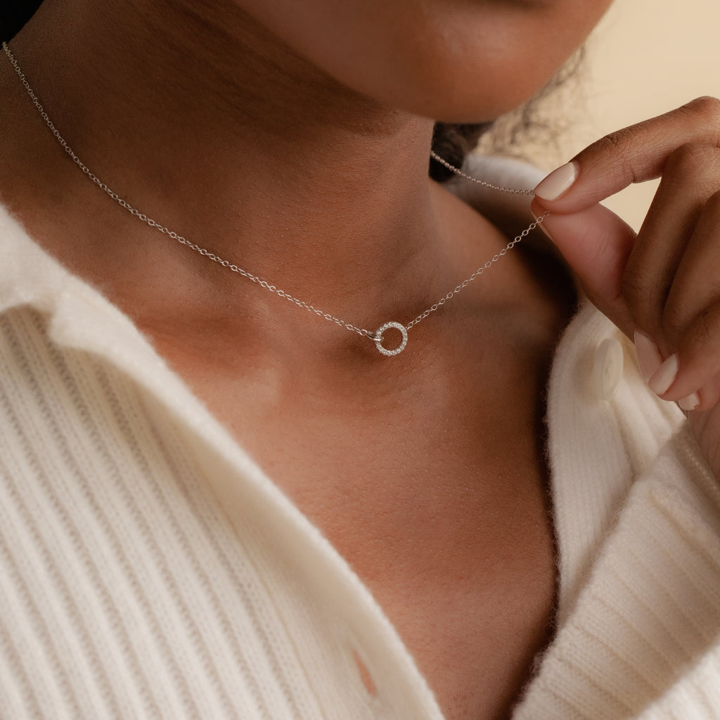 A person wearing a cream ribbed shirt and an elegant Pave Interlocking Necklace in Silver, featuring a delicate small circular pendant.