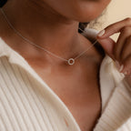 A person wearing a cream ribbed shirt and an elegant Pave Interlocking Necklace in Silver, featuring a delicate small circular pendant.