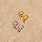 A pair of Shark Tooth Huggies in Silver, featuring pointed pendants, rests on a beige textured surface—perfect hoop earrings for your next beach vacation.