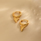 The Shark Tooth Huggies in 18K Gold feature small, shiny, pointed heart-shaped pendants—perfect, playful earrings for your next beach vacation.