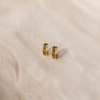 The Genevieve Peridot Huggies are small gold hoops with embedded peridot stones, perfect for adding a subtle sparkle to any look.