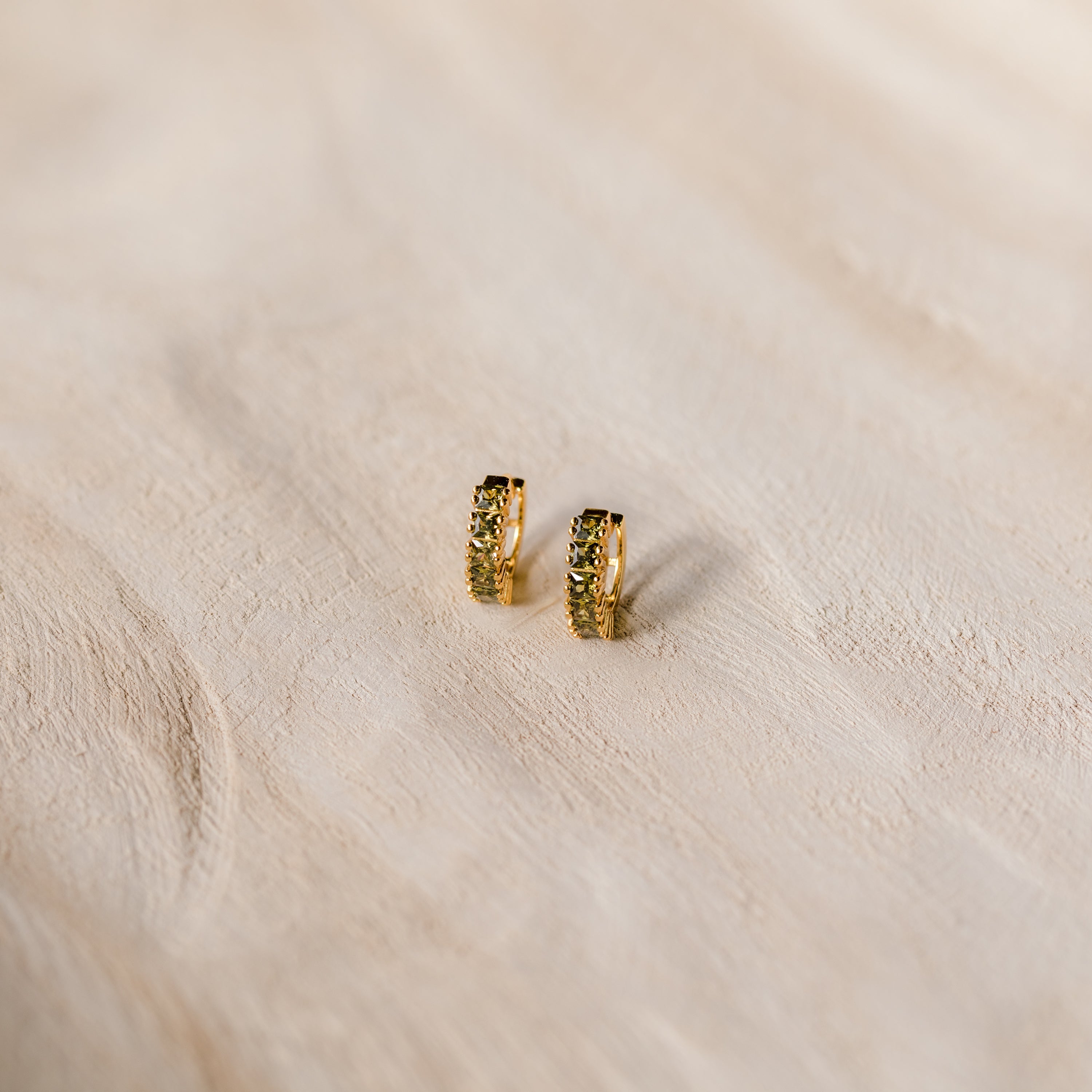 The Genevieve Peridot Huggies are small gold hoops with embedded peridot stones, perfect for adding a subtle sparkle to any look.
