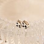 Add flair to any look with our stylish Checkered Huggies—silver hoop earrings featuring a bold black and white checker pattern. Displayed elegantly on clear textured glass.