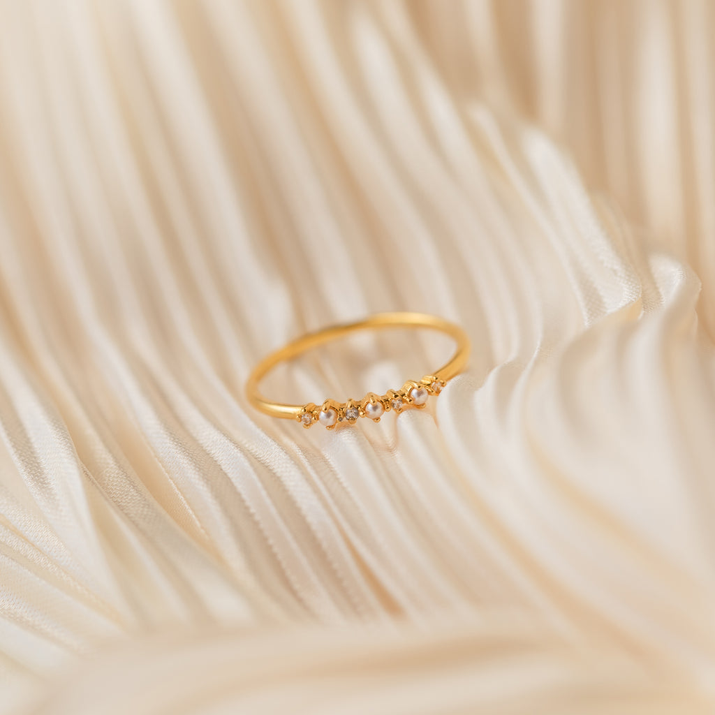 The Delicate Pearl Diamond Ring, accented with small diamonds, is displayed on soft, cream-colored fabric.
