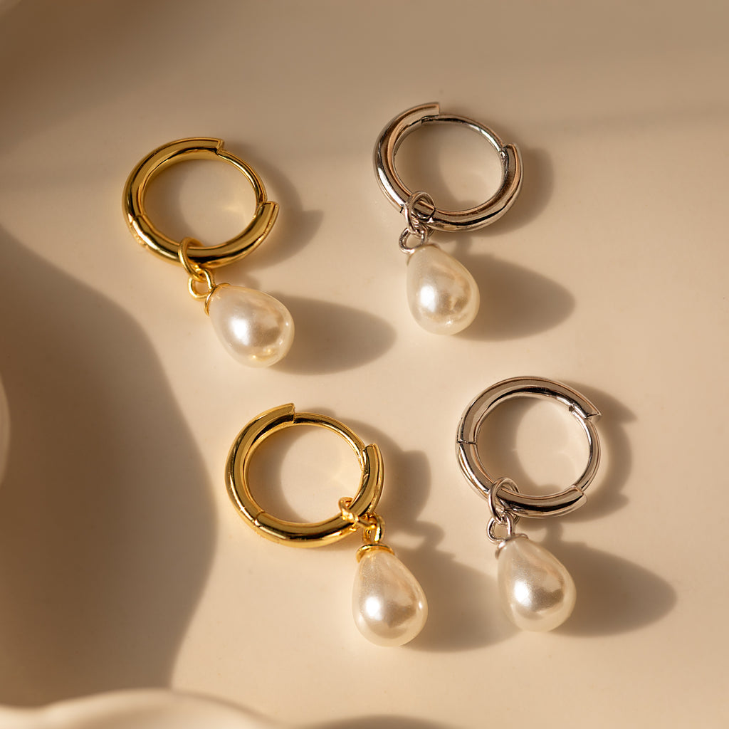 Two pairs of elegant earrings—one in 18K gold, one in silver—each featuring a dainty teardrop pearl. The Dainty Pearl Drop Huggies in 18K Gold are perfect to elevate any look.