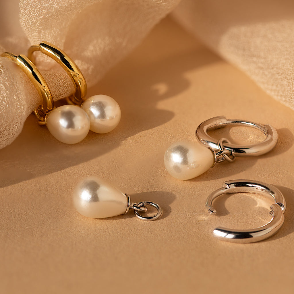 Dainty Pearl Drop Huggies—gold and silver hoops adorned with pearl charms—add elegant sophistication to any look. Displayed on a beige fabric background, these delicate earrings are perfect for chic styling.