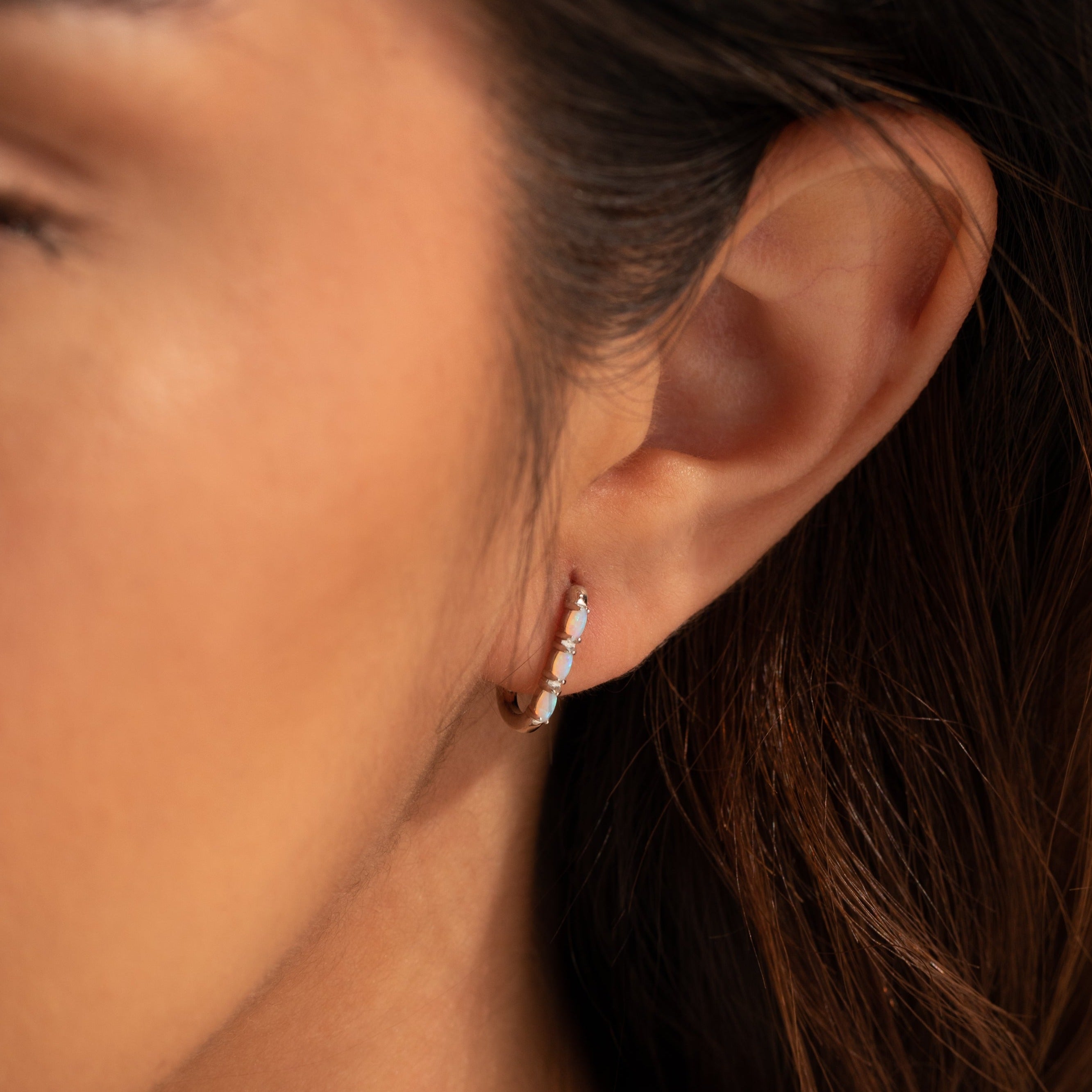 Close-up of a woman's ear wearing Halo Opal Hoops, minimalist gold huggie earrings adorned with delicate white opal stones.