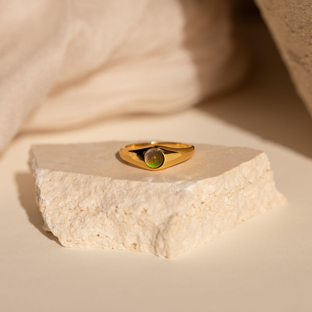 The Signet Mood Rings Set features gold rings with green gemstones, displayed on a light stone slab against a neutral backdrop for a nostalgic jewelry statement.