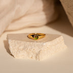The Signet Mood Rings Set features gold rings with green gemstones, displayed on a light stone slab against a neutral backdrop for a nostalgic jewelry statement.