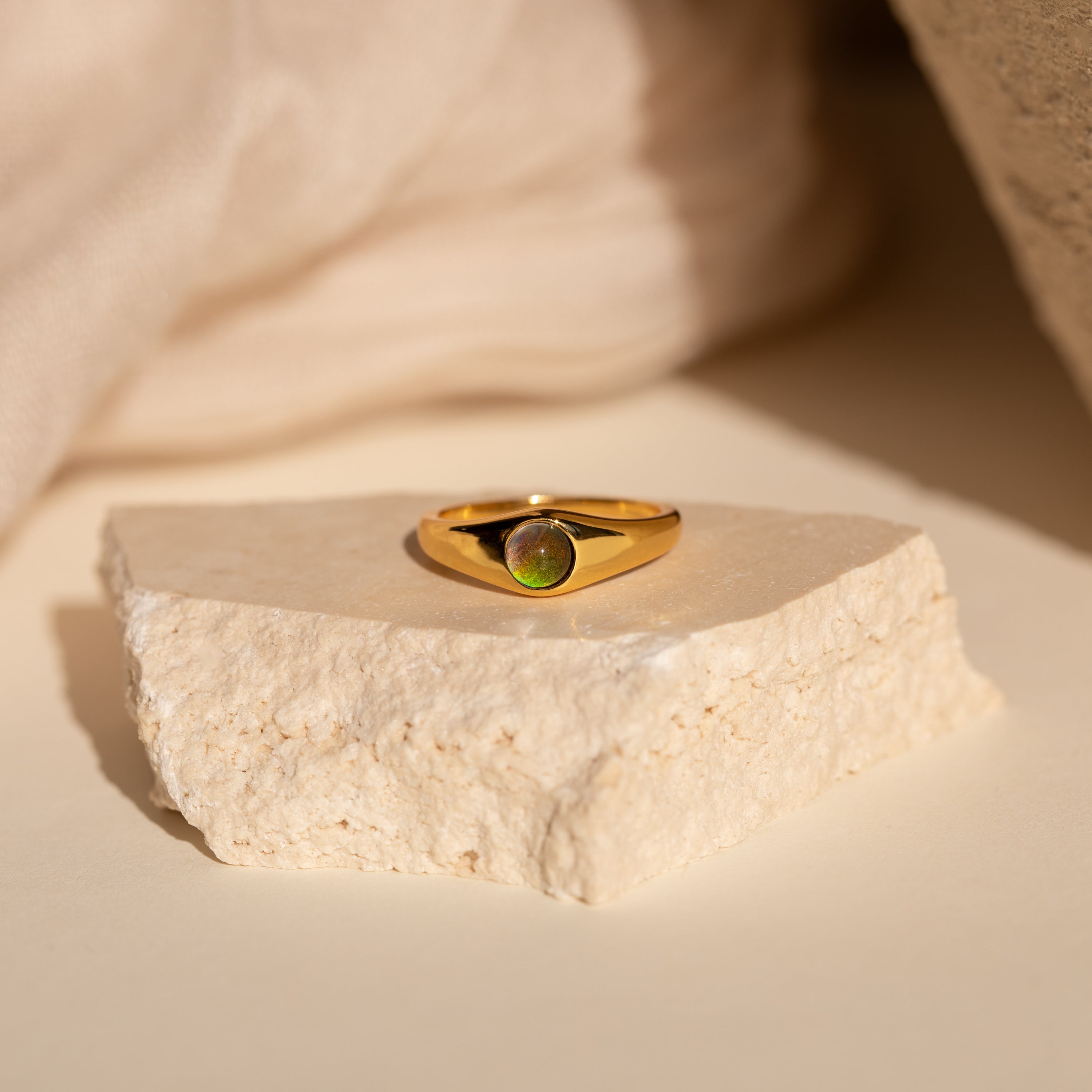 The Signet Mood Rings Set features gold rings with green gemstones, displayed on a light stone slab against a neutral backdrop for a nostalgic jewelry statement.