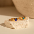 The Signet Mood Rings Set features two gold rings with blue and green stones, displayed on a cream stone slab—nostalgic, color-changing jewelry that captures mood magic.