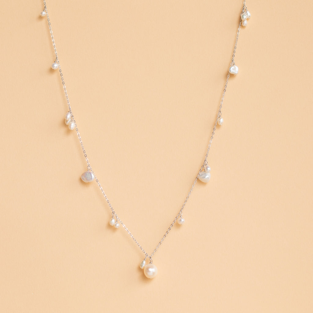 The Baroque Pearl Station Necklace in Sterling Silver, a delicate minimalist piece ideal for wedding jewelry, is displayed on a light beige background.