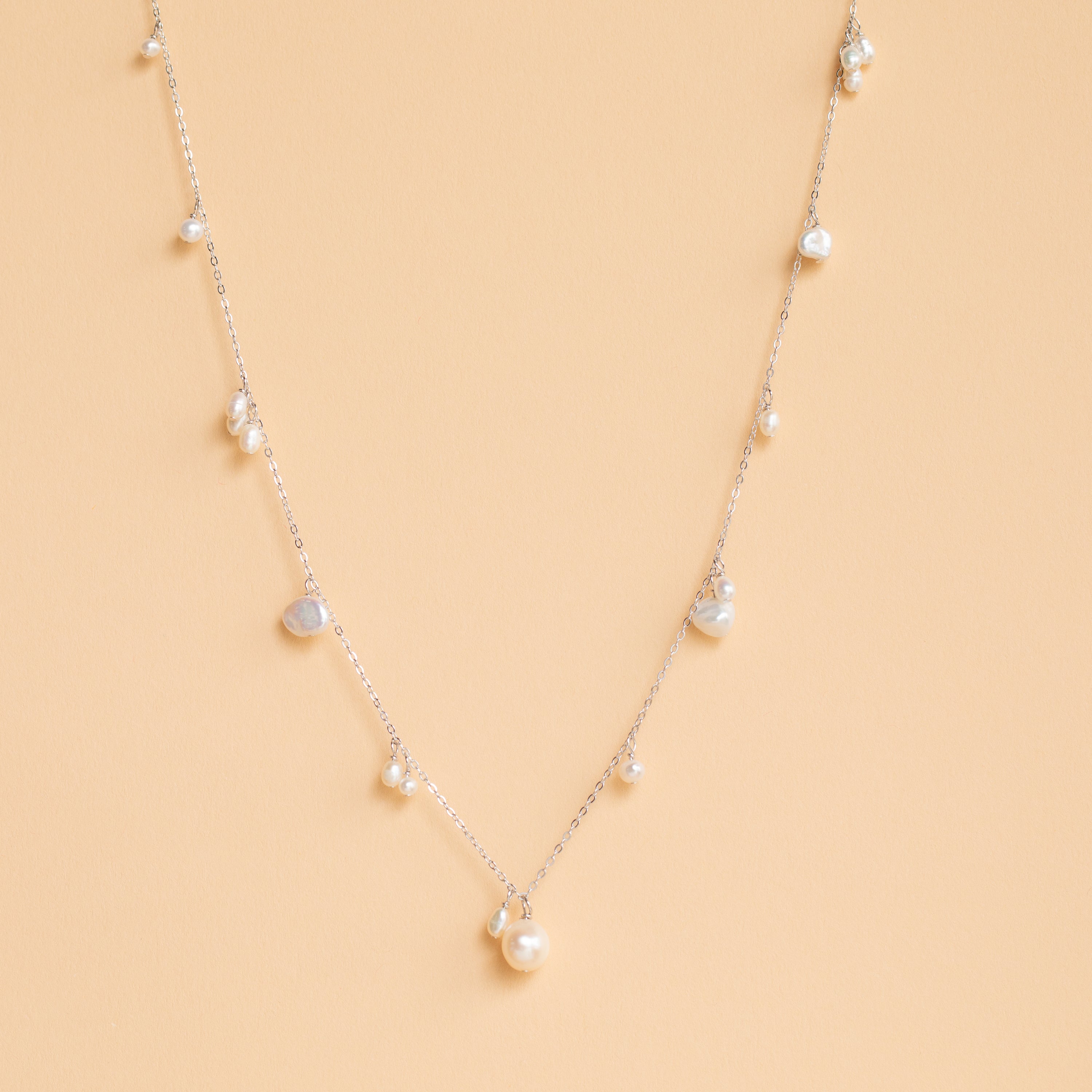 The Baroque Pearl Station Necklace in Sterling Silver, a delicate minimalist piece ideal for wedding jewelry, is displayed on a light beige background.
