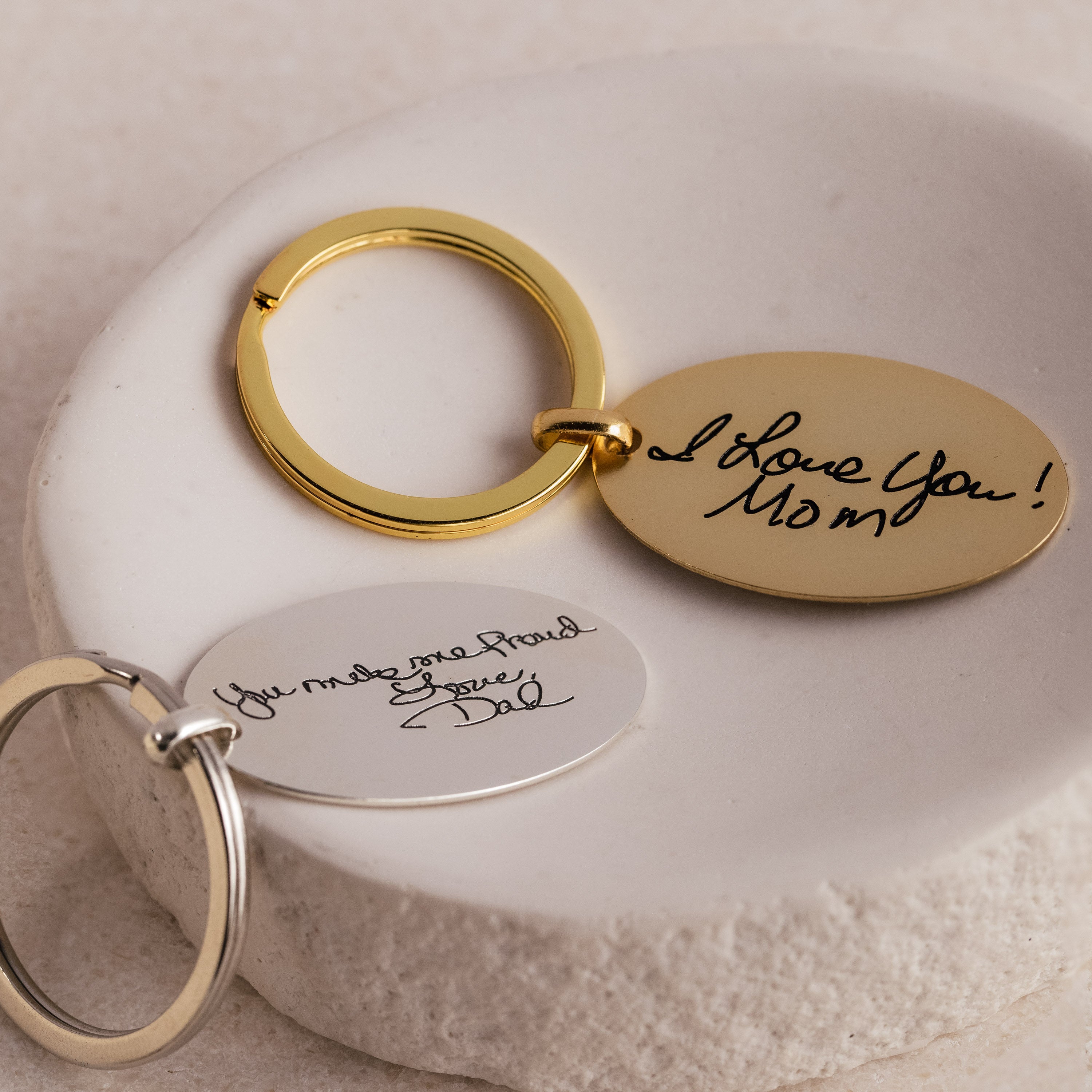 Two Handwriting Oval Keychains with engraved messages: "I Love You Mom!" and "You make me proud. Love, Dad"—perfect personalized keepsakes for your loved ones.