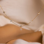 The Ivy Diamond Station Necklace in 18K Gold features small diamond accents, beautifully displayed on a soft beige fabric background.