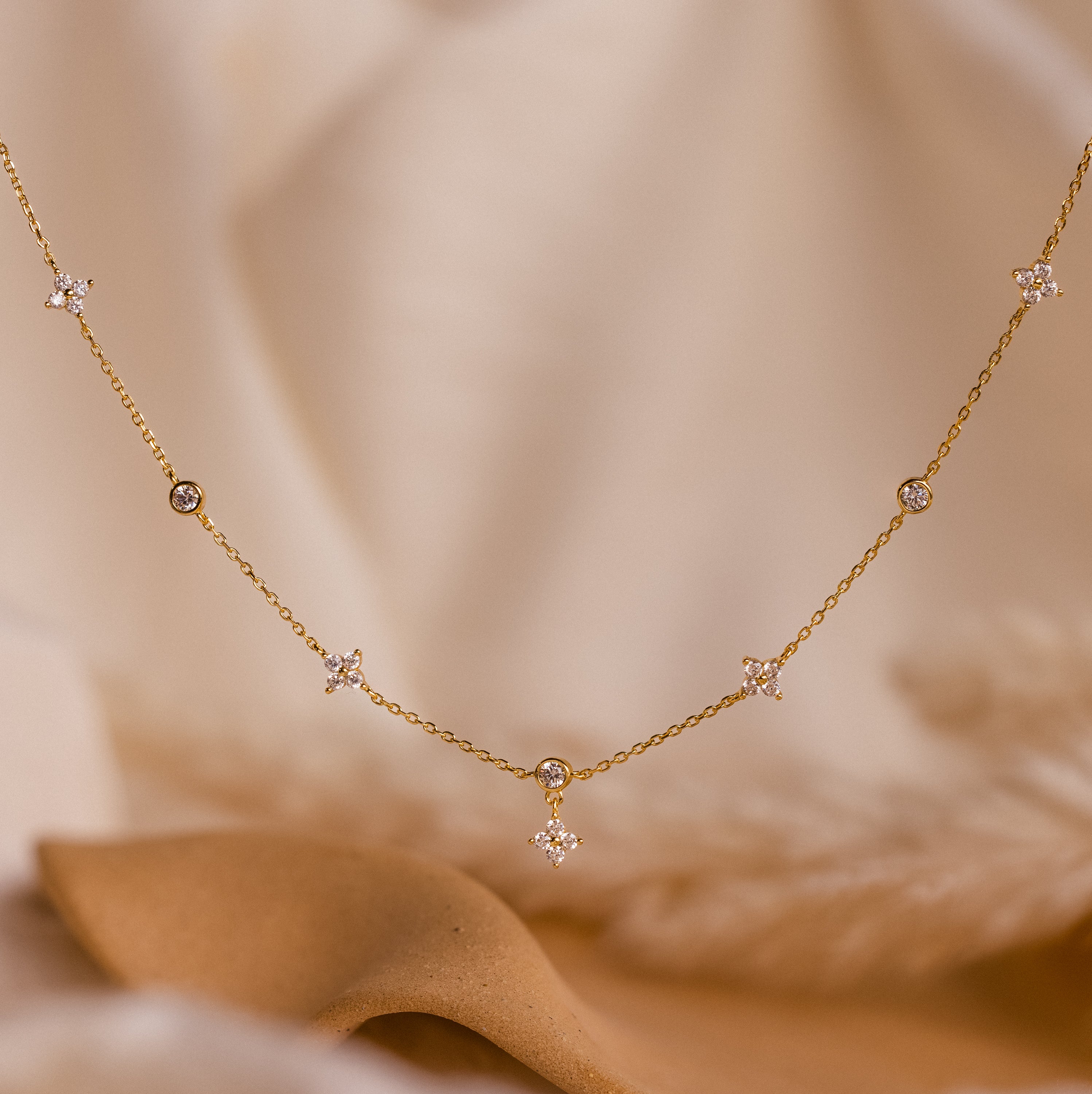 The Ivy Diamond Station Necklace features small star and round diamond accents, beautifully displayed on a soft beige fabric background.