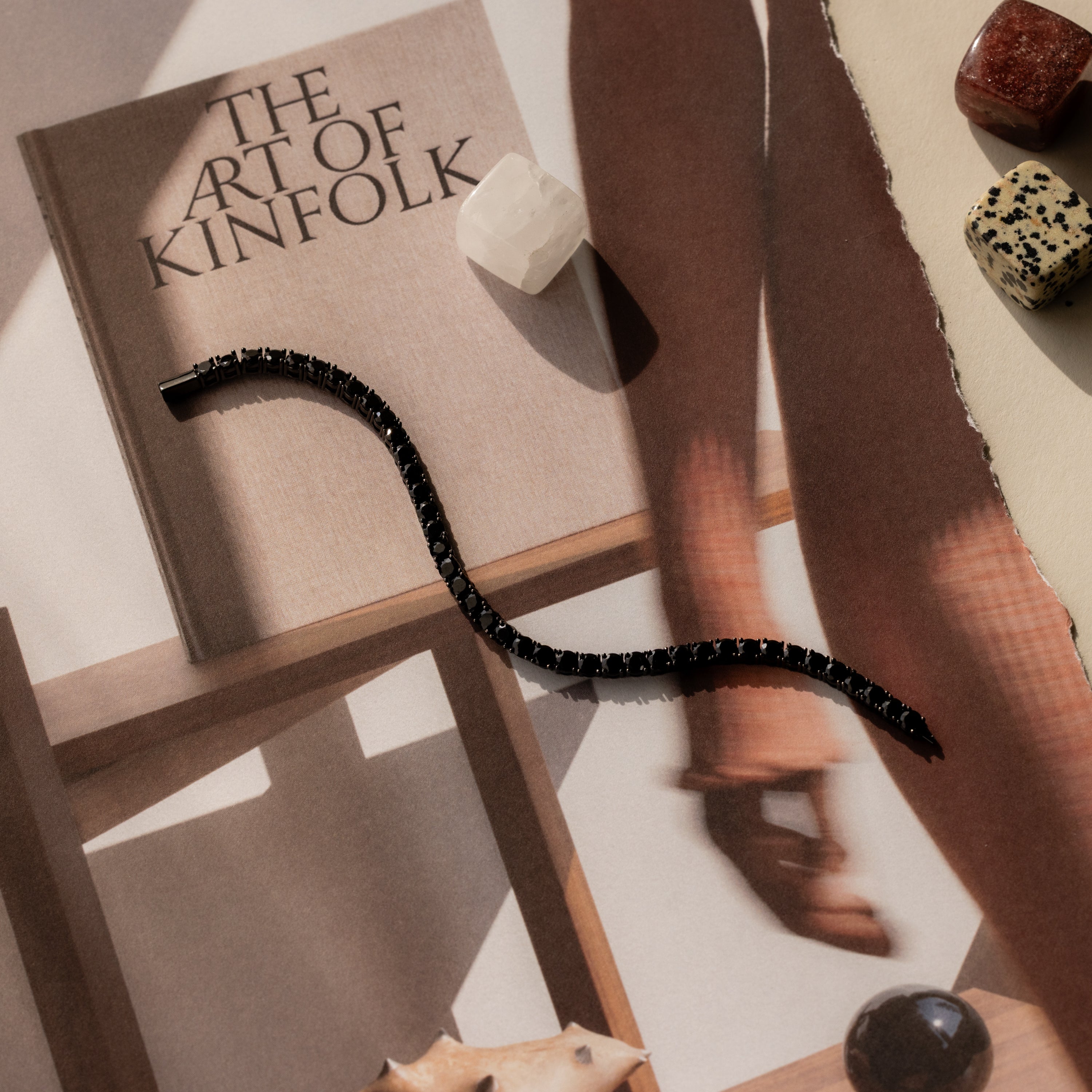 An Onyx Tennis Bracelet rests on a magazine titled “The Art of Kinfolk,” surrounded by crystals and soft shadows.