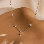 The Ivy Diamond Station Necklace features small crystals, flower-shaped charms, and diamond accents, elegantly displayed on a curved tan surface.