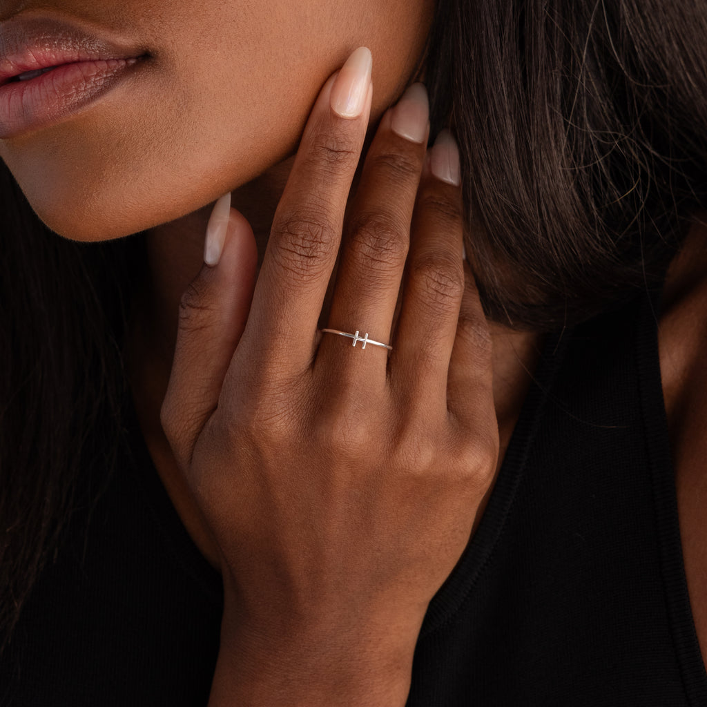 A woman with long nails gently touches her face while wearing the Alex Dainty Letter Ring in Sterling Silver, a thin, elegant personalized ring featuring a horizontal bar for a sophisticated touch.