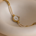 Beaded Pearl Timepiece in 18K Gold displayed on a smooth, cream-colored curved surface.