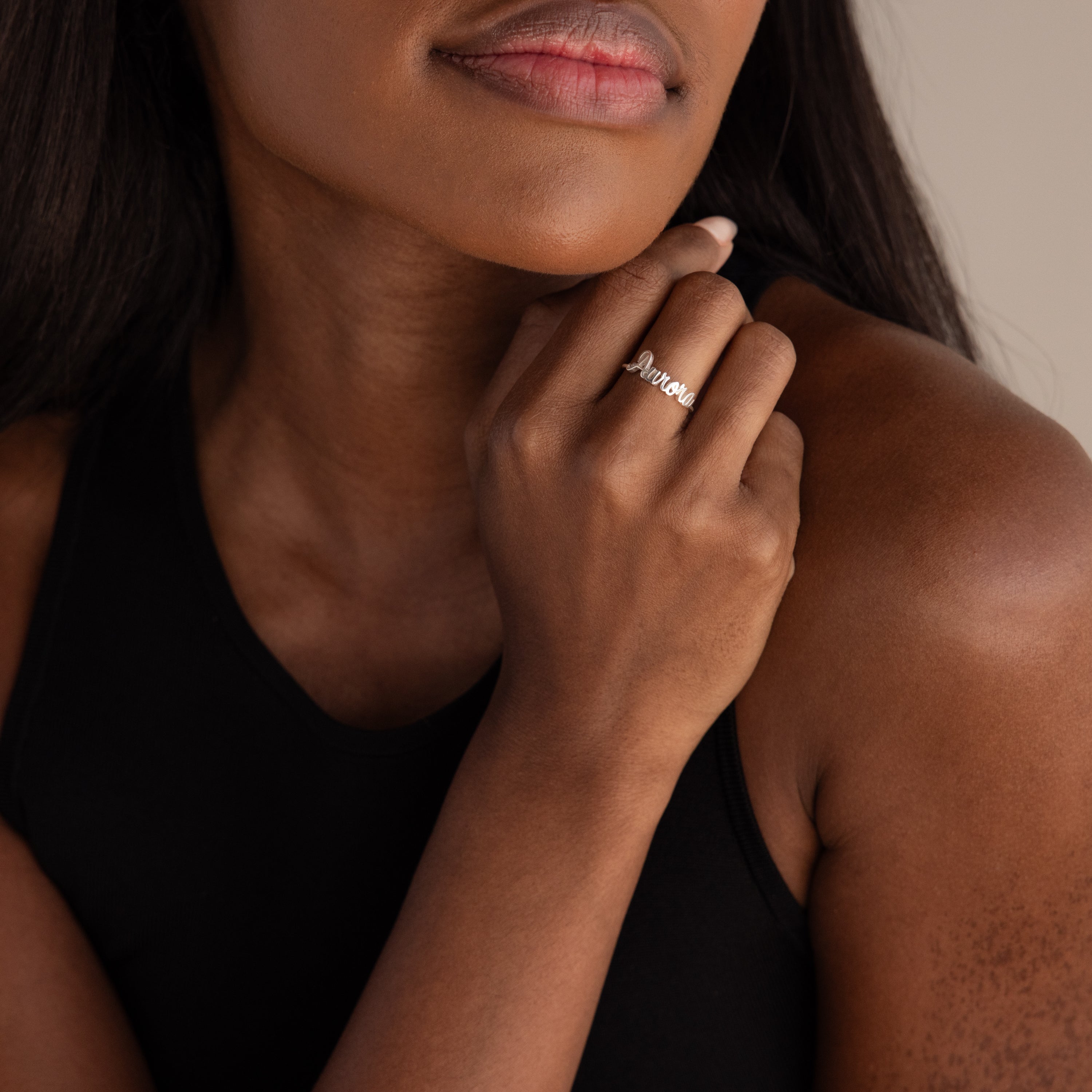 A woman in a black top touches her chin, displaying the Grace Script Name Ring in Sterling Silver with "amour" elegantly written on her finger.