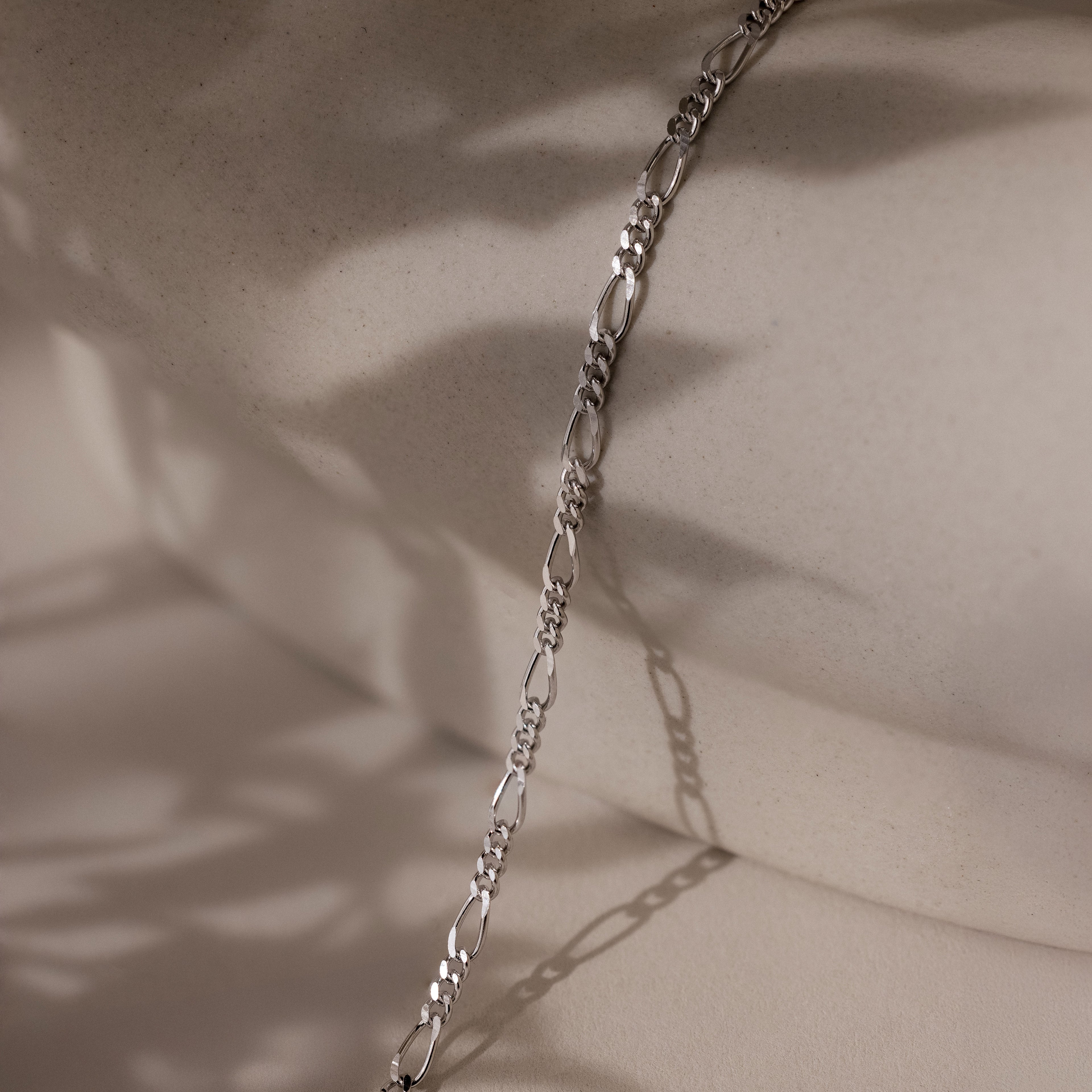 Silver chain on a beige surface with soft shadows