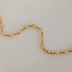 An elegant jewelry piece, the Eternity Pearl Bracelet in 18K Gold features white pearls in a wavy pattern on a light beige background.