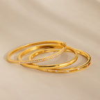 Three Lace Diamond Bangles in Sterling Silver, featuring an open station design with round diamonds, are elegantly arranged on a beige surface.