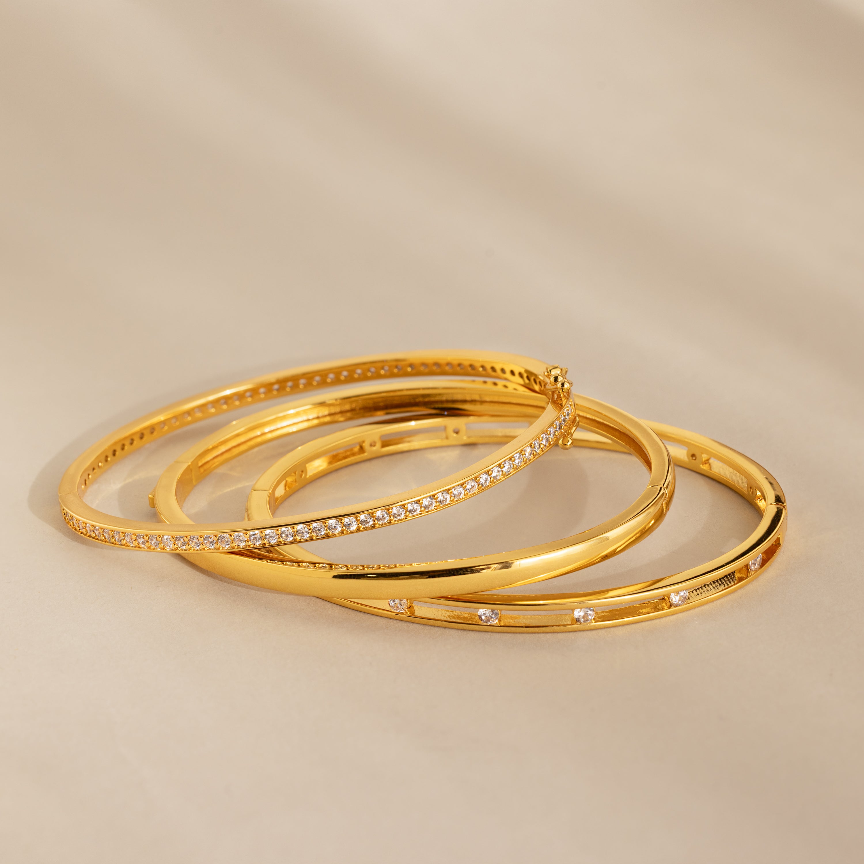 Three Lace Diamond Bangles in Sterling Silver, featuring an open station design with round diamonds, are elegantly arranged on a beige surface.