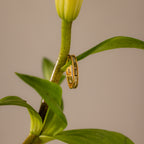 The Peridot Inlay Eternity Ring with rectangular gold green stones rests on the stem of a green plant topped with a yellow bud.