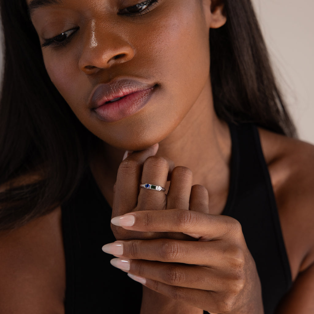 A woman with long hair in a black top touches her chin, displaying the Bold Birthstone Signet Ring in Sterling Silver on her finger.
