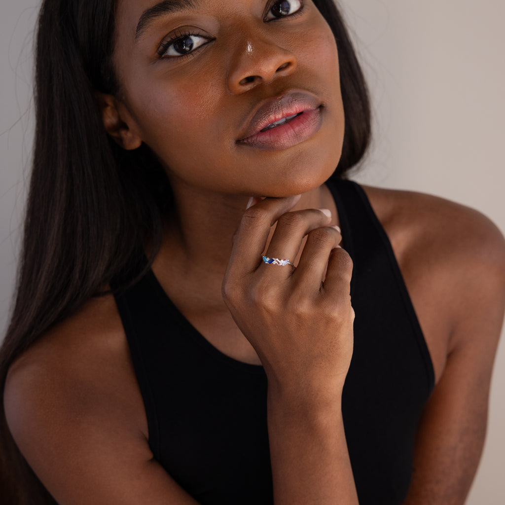Woman in a black top touches her chin, thoughtfully gazing at the camera while wearing the Cluster Baguette Birthstone Ring in Sterling Silver.