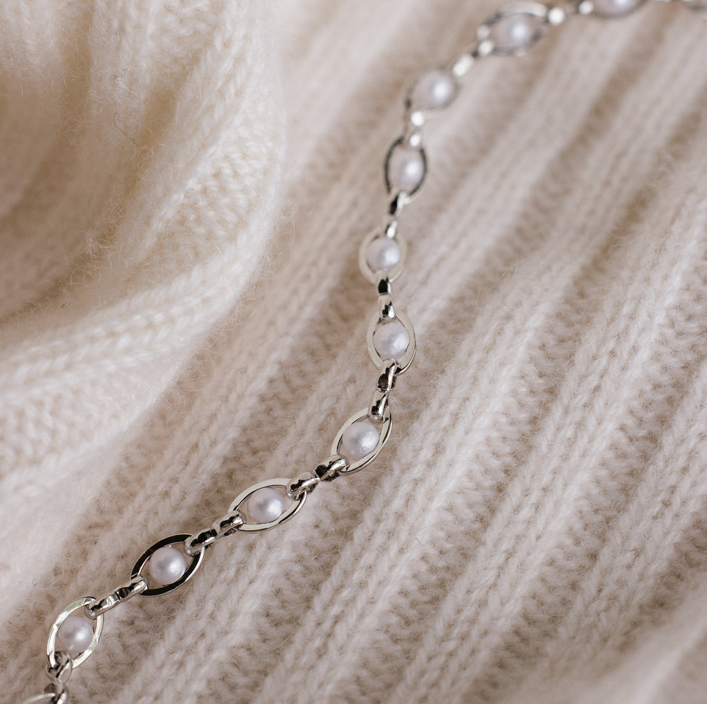 The Eternity Pearl Bracelet in Sterling Silver is displayed on a cream-colored, ribbed knit fabric, highlighting the elegant design and timeless beauty of this jewelry piece.