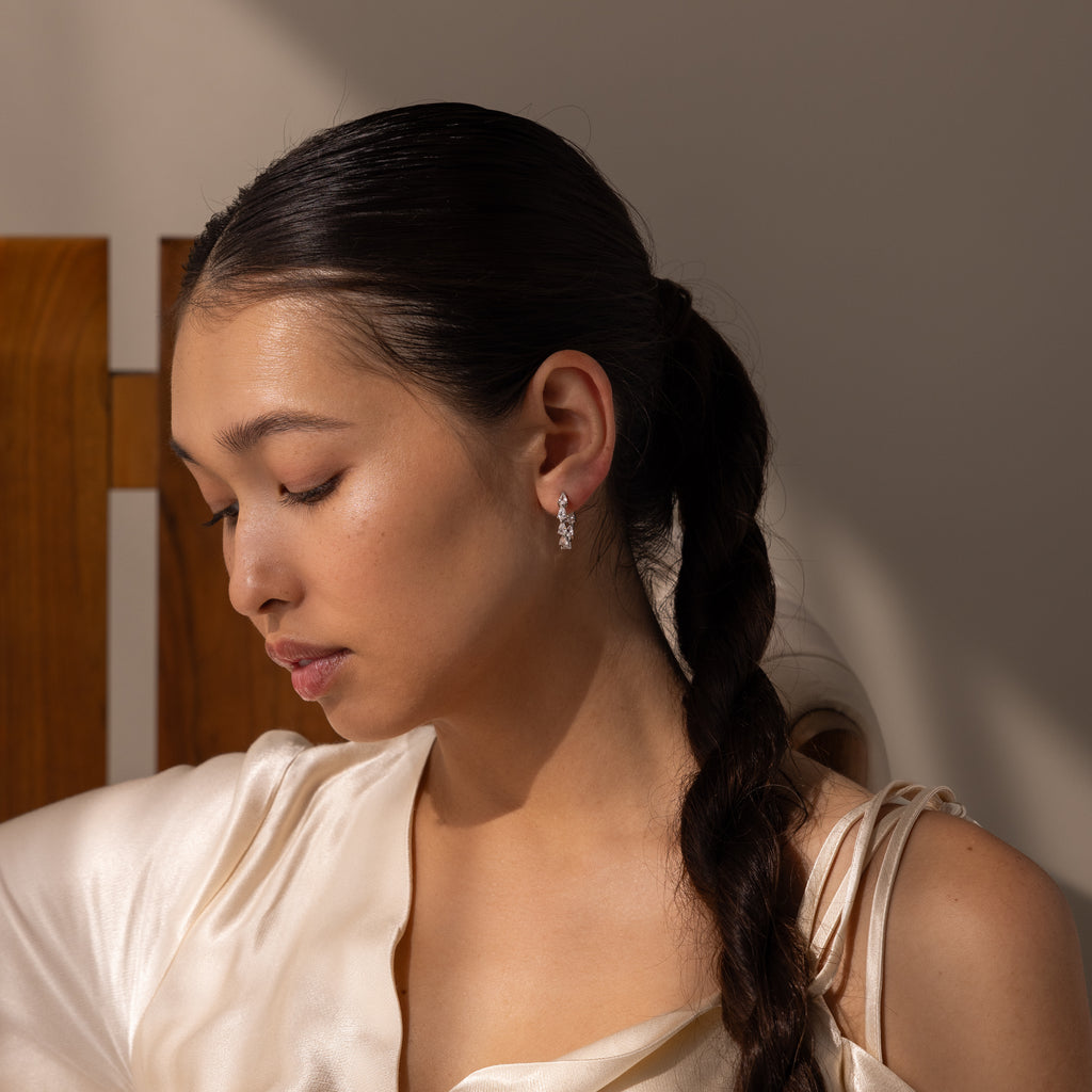 Woman with long dark braid wearing a cream satin top and Inside Out Pear Diamond Hoops in Silver, sitting with eyes closed in soft light—a perfect bridesmaid gift.