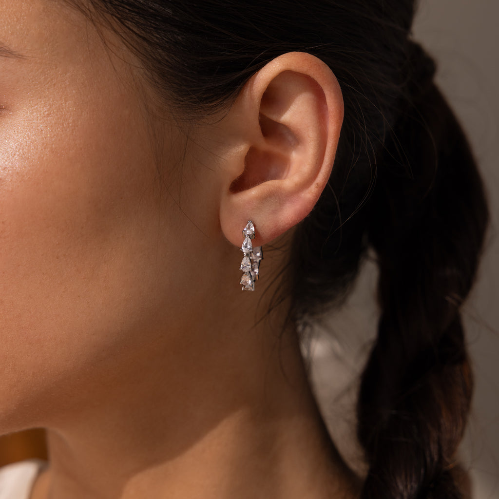 A close-up of a womans ear wearing Inside Out Pear Diamond Hoops in Silver—elegant earrings with sparkling gems, perfect as a bridesmaid gift.
