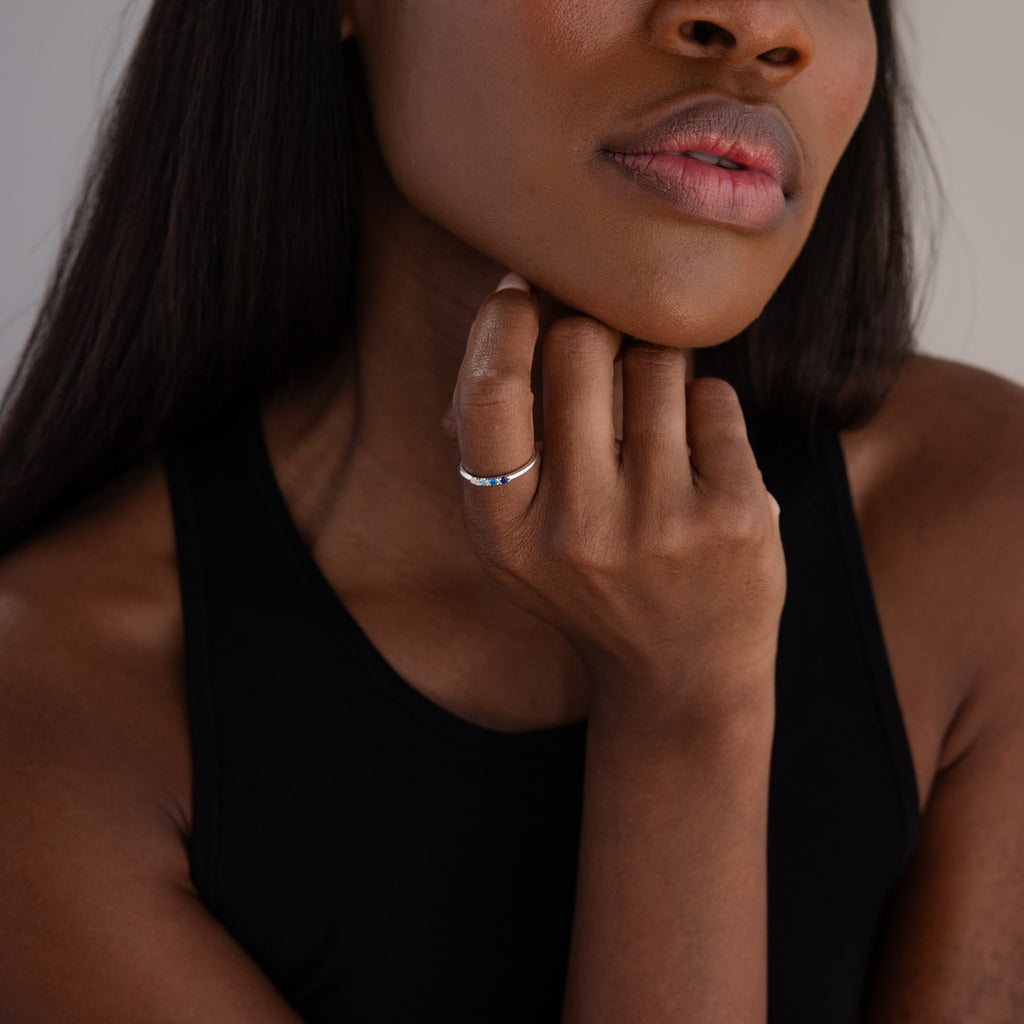 A woman wearing a sleeveless black top rests her chin on her hand, showing off the Mini Birthstone Ring in Sterling Silver—her personalized birthstone ring catches the light.