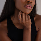 A woman wearing a sleeveless black top rests her chin on her hand, showing off the Mini Birthstone Ring in Sterling Silver—her personalized birthstone ring catches the light.