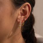 Close-up of a womans ear adorned with multiple gold and gemstone earrings, featuring statement hoops and sparkling Inside Out Pear Diamond Hoops.